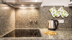 Una cocina con una campana de acero inoxidable, una placa de inducción integrada, un hervidor y un par de guantes de horno colgados en la pared.
