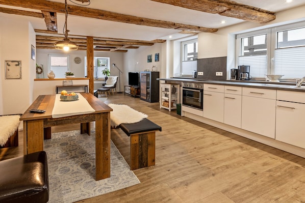 Une cuisine moderne avec des poutres en bois, un coin repas avec une table et un banc, et une vue sur le salon.