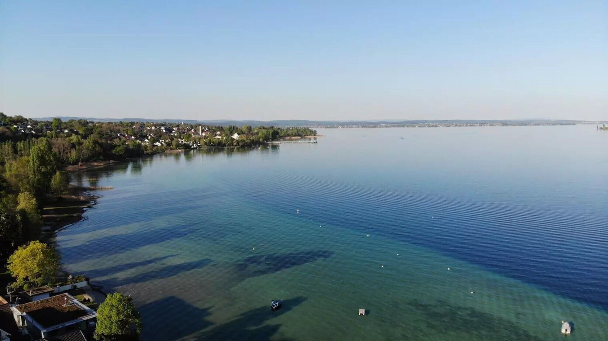 Un lac paisible aux eaux limpides, entouré d’un quartier résidentiel avec des maisons et des arbres.