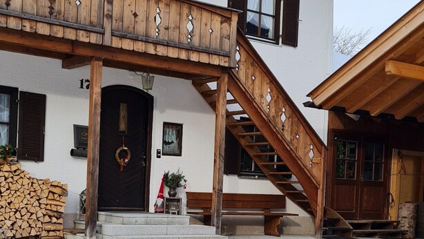 A building with a wooden staircase leading to a door, a snow-covered ground, and a brick-paved area. - Apartment 'Haus Bergblick' with Balcony and Wi-Fi (Mittenwald)
