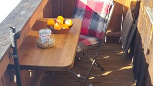 A wooden deck with a table and two wicker chairs with plaid cushions. - Apartment 'Haus Bergblick' with Balcony and Wi-Fi (Mittenwald)