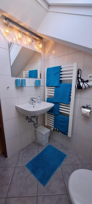 A bathroom with a white sink, mirror, towel rack, and a blue mat on the floor.