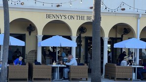 Ulkoterassi, jossa on rottinkihuonekaluja ja aurinkovarjoja, kuuluu ravintolaan nimeltä ”Benny’s on the Beach”.