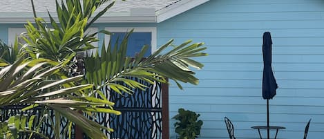 Una casa azul claro con techo inclinado, un patio con mesa y sillas, y un paraguas grande.