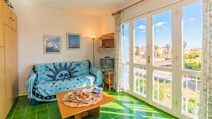 A room with a sofa, a television, a table with food, and large windows.