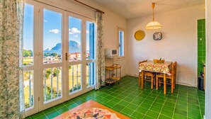 A room with a dining table, chairs, a microwave, a clock, and a view through large windows.