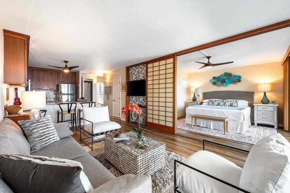 A spacious living area with a sofa, coffee table, and a dining area with chairs and a kitchen in the background.