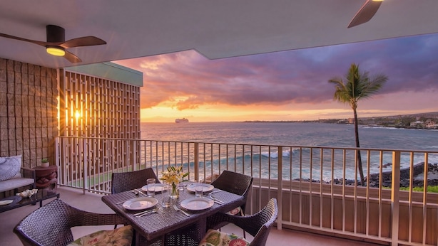 Ein Balkon mit einem Tisch für zwei Personen, mit Blick auf einen Sonnenuntergang über dem Meer.