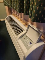 Calentador portátil con panel de control, situado en el suelo junto a una ventana con cortinas decoradas.