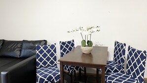 Un salón con un sofá de cuero negro, sillas con estampado azul, una mesa de madera y una cesta de mimbre con flores blancas.