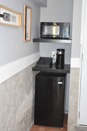 Compact kitchenette with a refrigerator, microwave, and coffee maker, perfect for preparing a quick meal.
