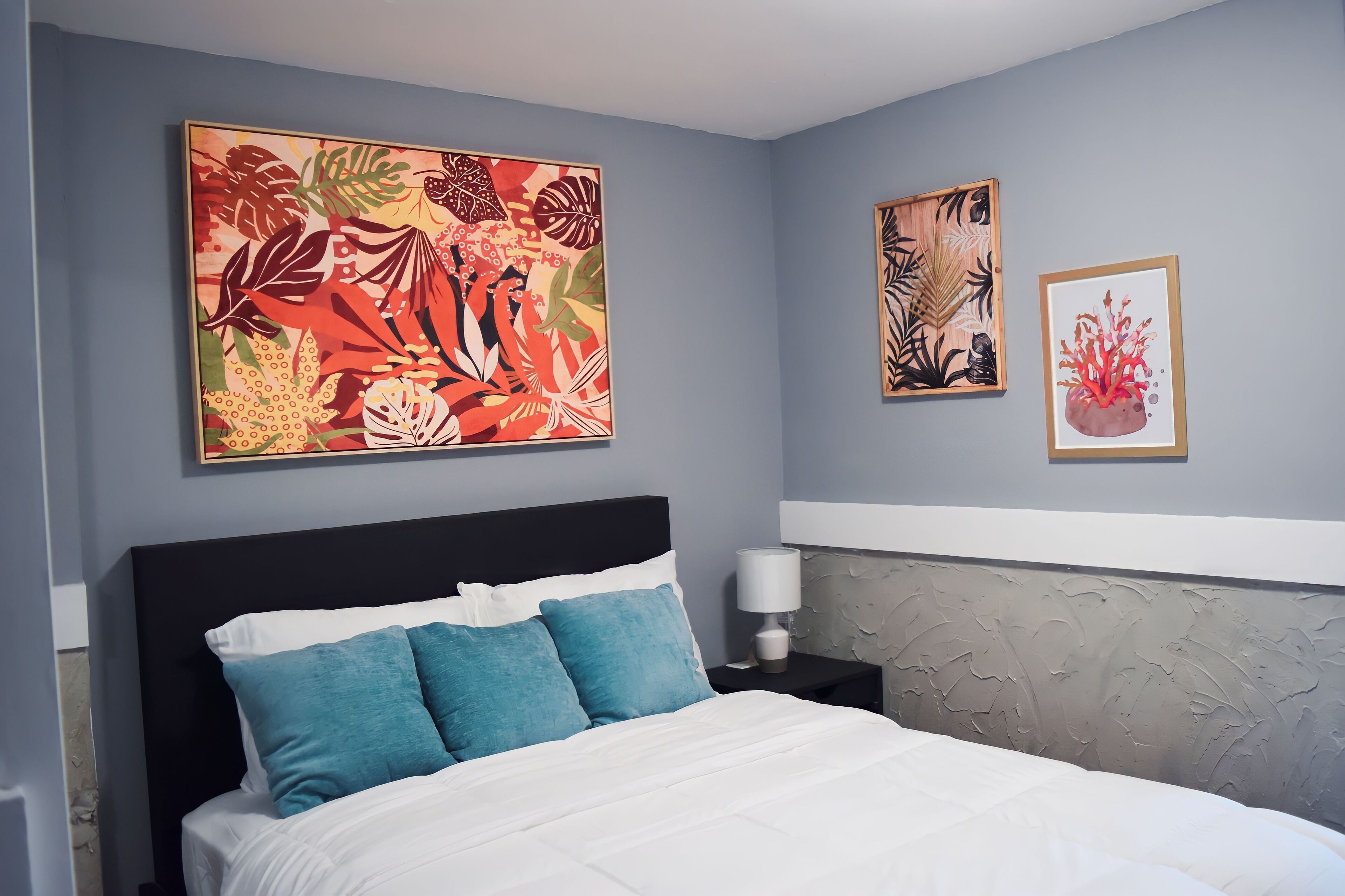 Ein Schlafzimmer mit einem Bett, einem Nachttisch und zwei an der Wand befestigten Kunstwerken.