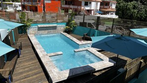 A rectangular pool with a wooden deck and a stone border.