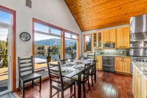 Uma sala de jantar com vista para montanhas e um lago, teto de madeira e eletrodomésticos de cozinha modernos.