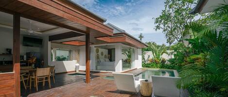 A modern outdoor patio with a pool, wooden deck, and lush greenery.