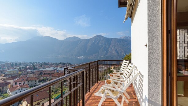 Un balcon avec des chaises blanches, une vue sur les montagnes et une ville en contrebas.