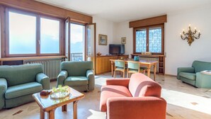 Un salon avec des canapés verts, une table basse en bois, un téléviseur et un coin cuisine comprenant une table à manger et des chaises.