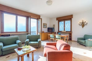A living room with green sofas, a wooden coffee table, a television, and a kitchen area with a dining table and chairs. - GuestHost - Bright villa with lake view, can accommodate up to 6 people.The property is located in a residential area of Mandello del Lario, a town on the shores of the Lecco branch of Lake Como.The area is ideal for both relaxing stays and trekking love (Mandello del Lario)