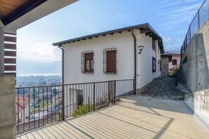 A balcony with a view of a town, a stone wall, and a building with a white facade and wooden shutters. - GuestHost - Bright villa with lake view, can accommodate up to 6 people.The property is located in a residential area of Mandello del Lario, a town on the shores of the Lecco branch of Lake Como.The area is ideal for both relaxing stays and trekking love (Mandello del Lario)