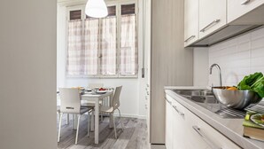 Een moderne keuken met een eethoek, witte kastjes en een raam met gordijnen.