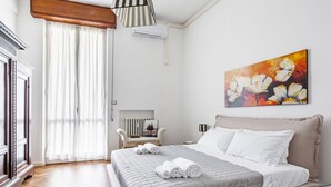 Een slaapkamer met een bed, een schilderij, een radiator en een raam met gordijnen.