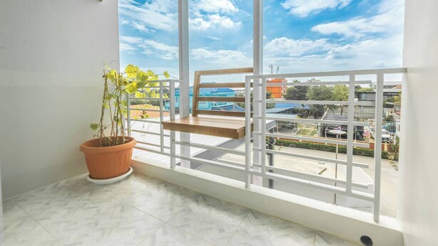 A balcony with a potted plant, a wooden shelf, and a view of buildings and a parking lot. - Sananwan Hometel (Bang Phli)