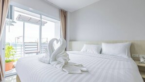 A hotel room with a large bed, a heart-shaped towel arrangement, a nightstand, and a view of the outdoors through a sliding glass door. - Sananwan Hometel (Bang Phli)