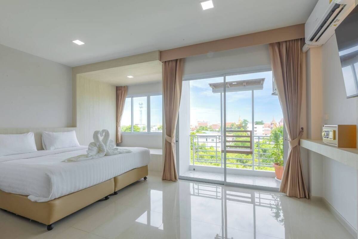 A modern hotel room with a large bed, a balcony with curtains, and a city view.
