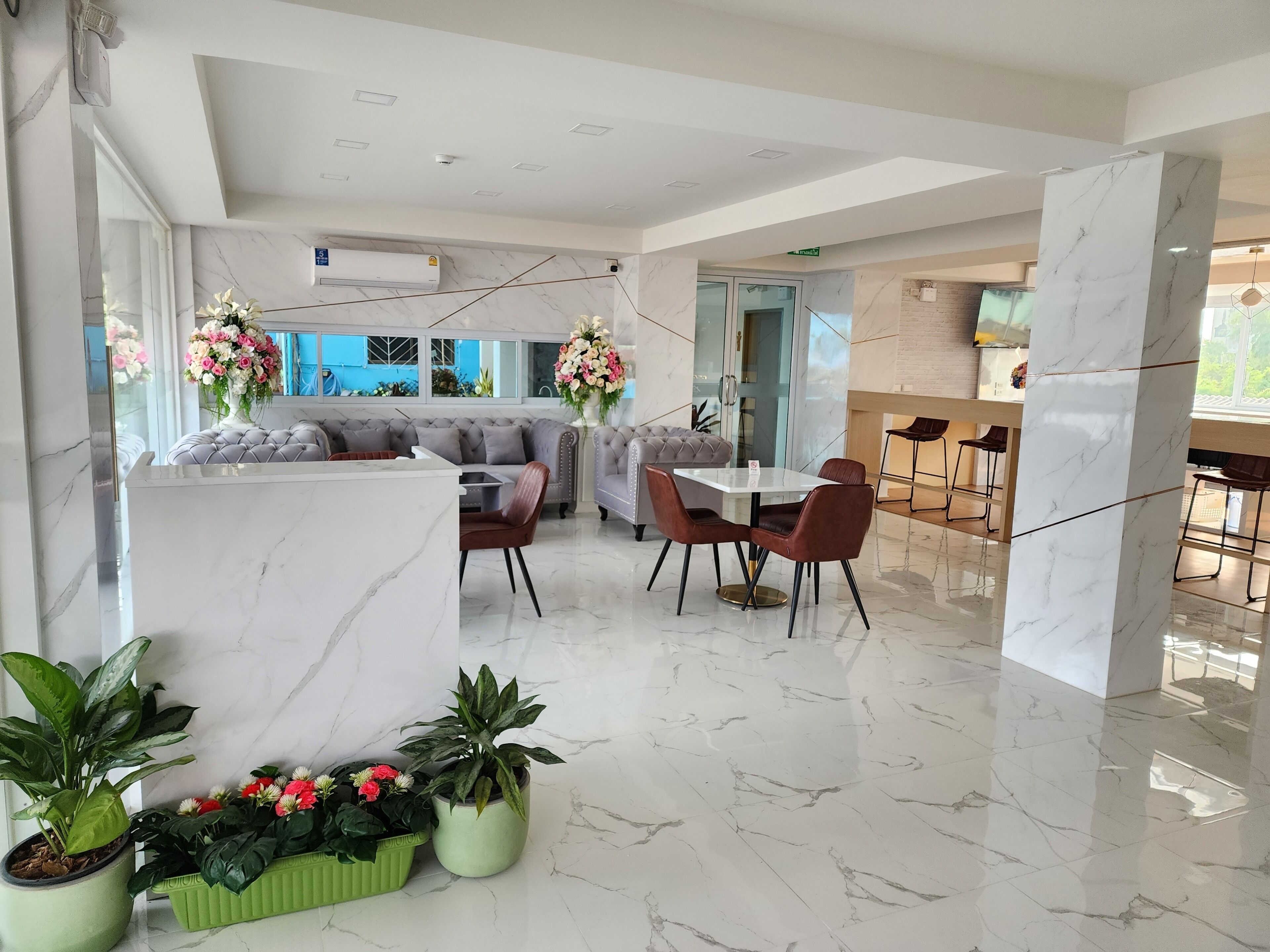 Un moderno vestíbulo de hotel con suelo de mármol, una zona de estar con sofás y sillones, y plantas en macetas.