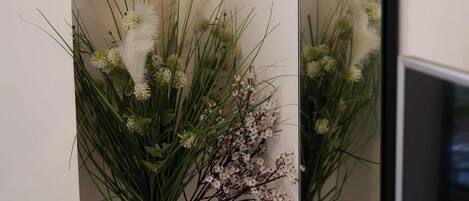 Rincón con un jarrón blanco que contiene un arreglo floral, un espejo y una superficie de madera.
