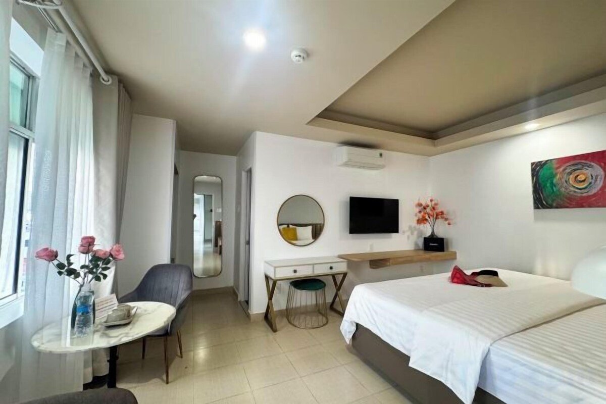 Habitación de hotel con cama, escritorio, silla, televisor y ventana con cortinas.