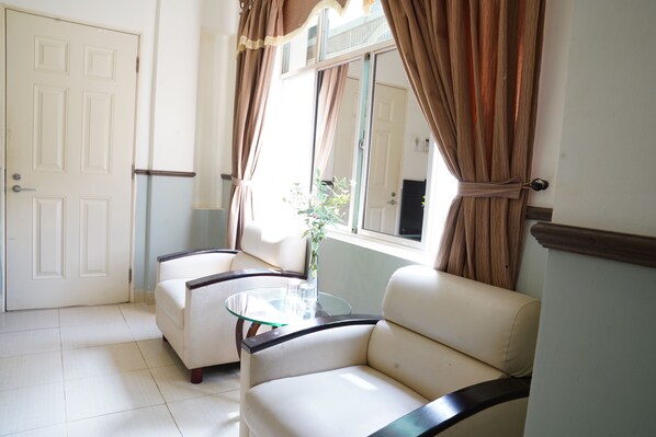 Um quarto com duas poltronas de couro branco, uma mesa de vidro e uma janela grande com cortinas.