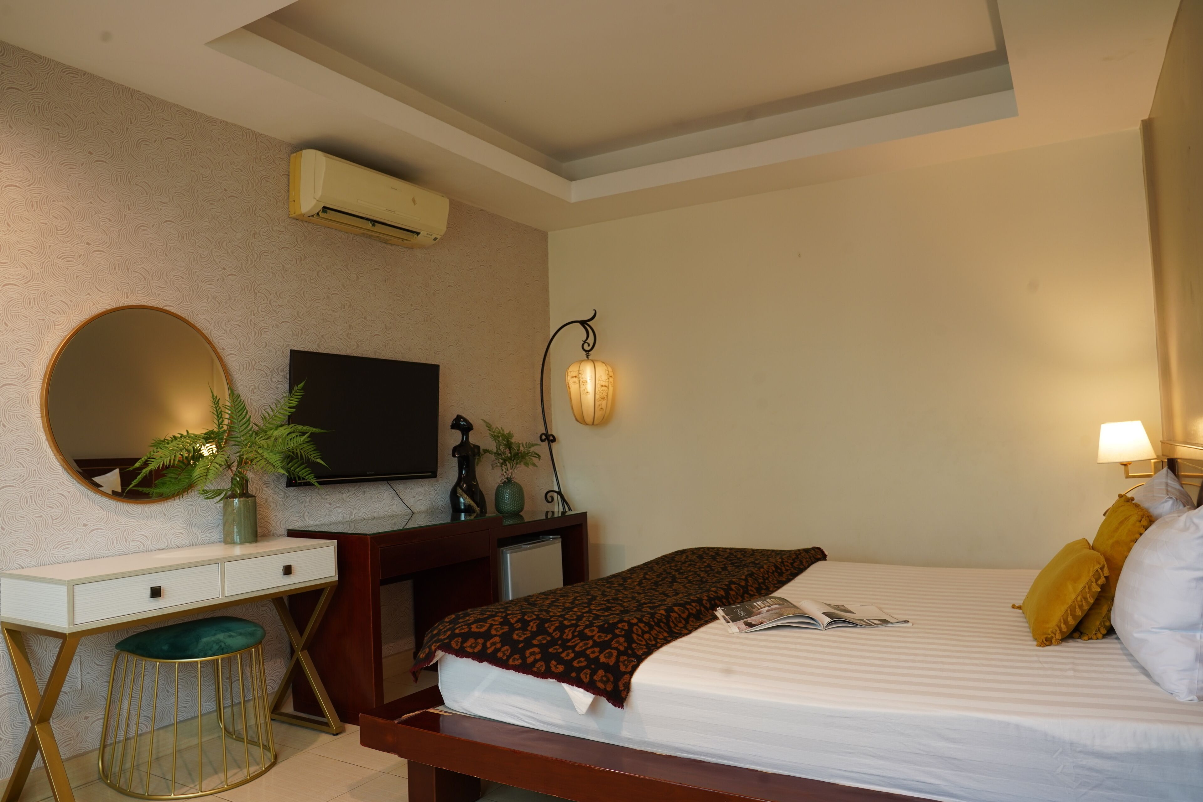A hotel room with a bed, bedside table, TV, and a desk with a chair.