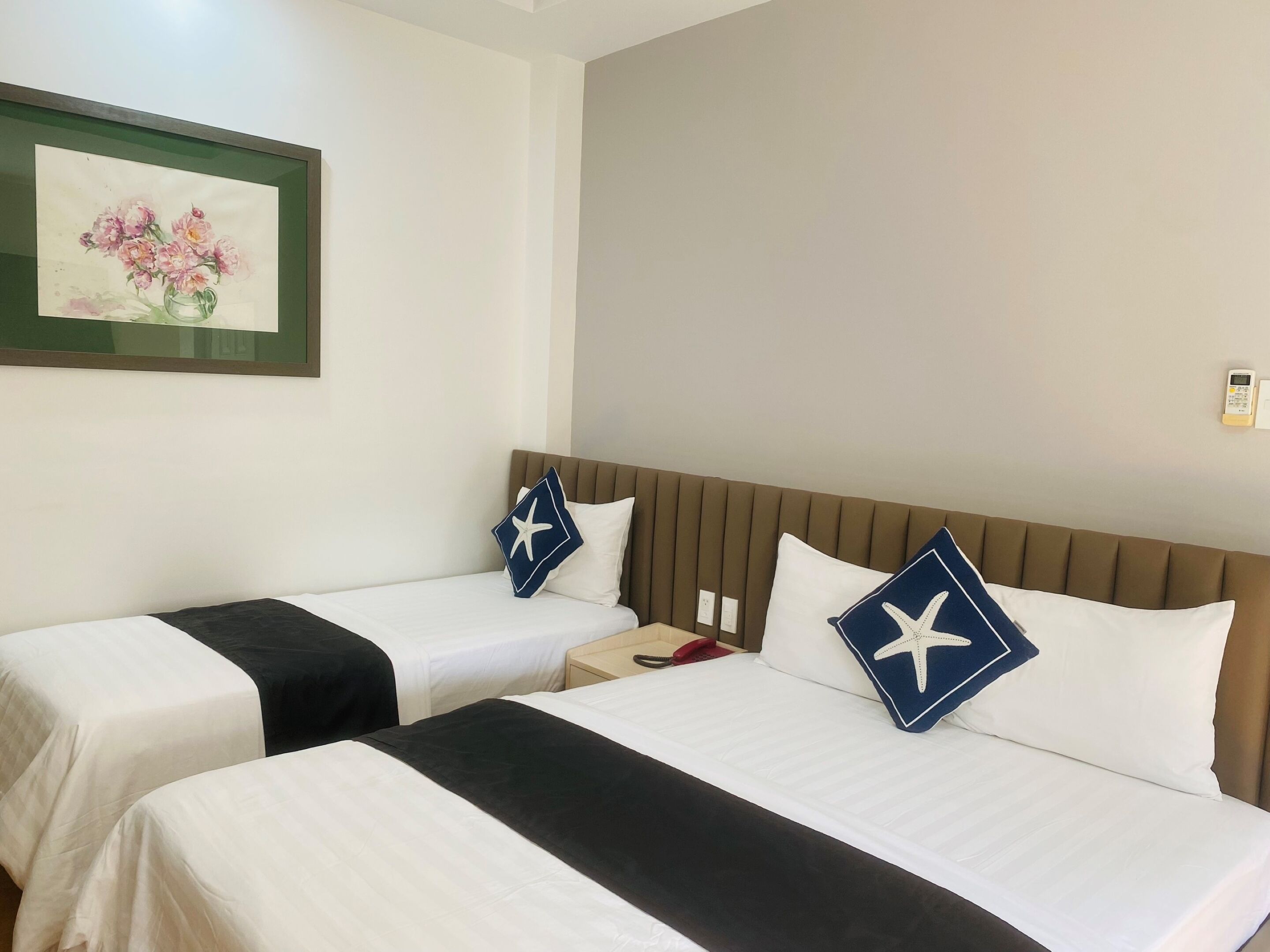 Hotelkamer met twee bedden, elk met witte beddengoed en zwarte accenten, een ingelijst bloemwerk op de muur, en een bruin hoofdeinde.