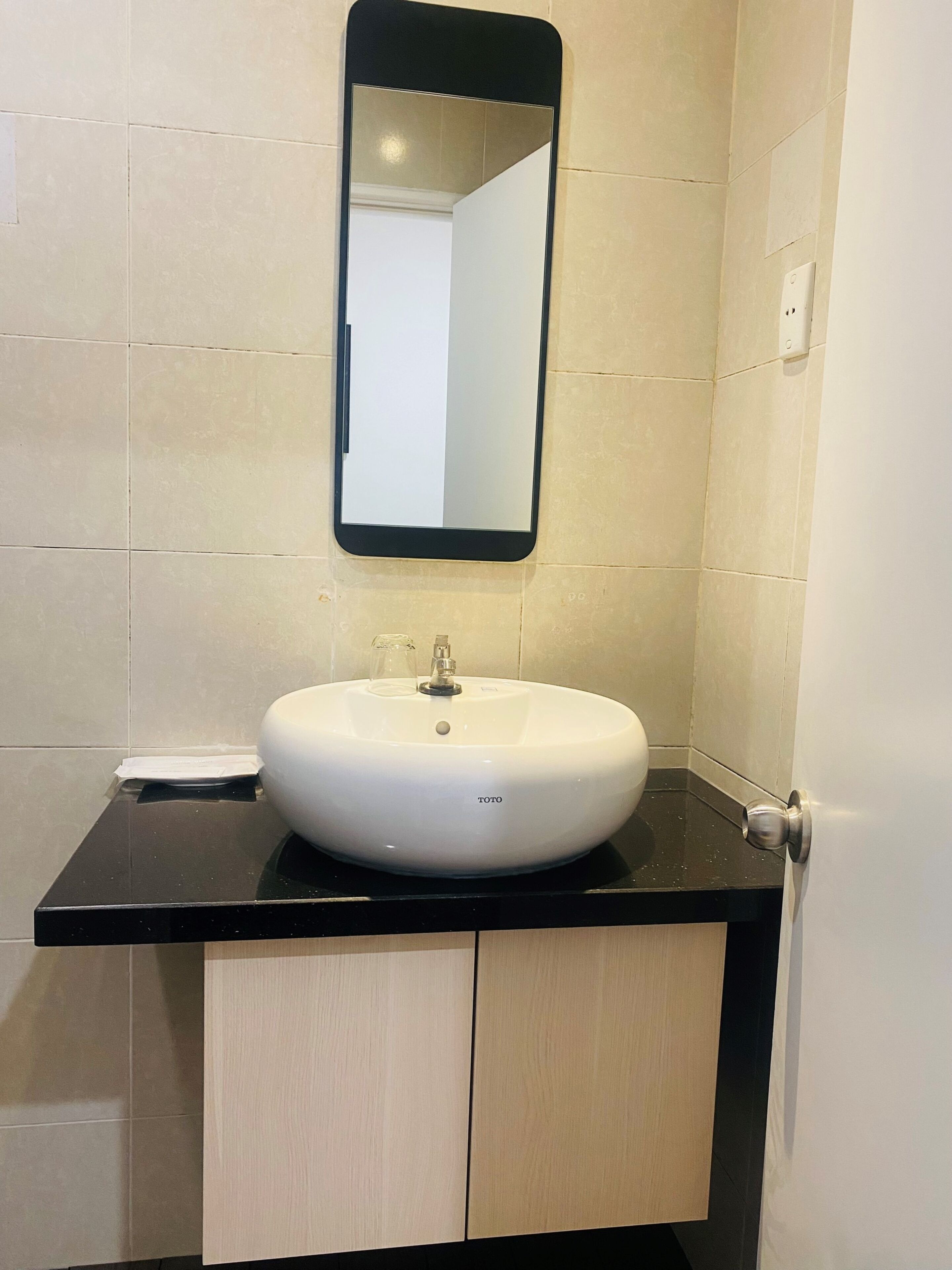 Une salle de bain avec un lavabo blanc, un plan de toilette noir et un miroir au-dessus.