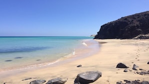 A beach with clear turquoise water, sandy shore, and rocky outcrops.