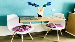 A dining area with two white chairs with purple cushions, a wooden table, and a vase with blue flowers.