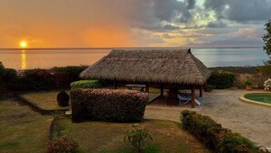 Une cabane au toit de chaume, dotée d’une piscine et offrant une vue sur l’océan au coucher du soleil.