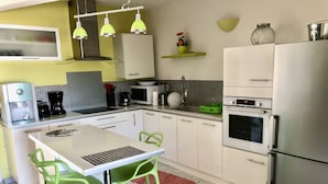 Une cuisine moderne avec un plan de travail blanc, des chaises vertes, un réfrigérateur en acier inoxydable et un four à micro-ondes.