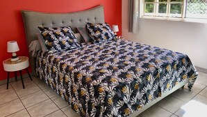 Un lit avec une couvre-lit à motifs floraux, une tête de lit rembourrée de couleur grise et une table de chevet avec une lampe.