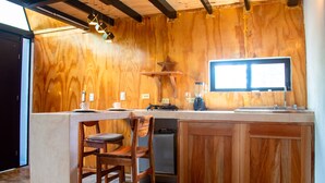 A kitchen with wooden walls, a built-in island, bar stools, a blender, and a window. - Cacao Cabin, Only Adults (El Cuyo)