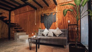 A cozy room with a grey sofa, patterned cushions, a woven rug, a potted plant, and a macrame wall hanging. - Cacao Cabin, Only Adults (El Cuyo)