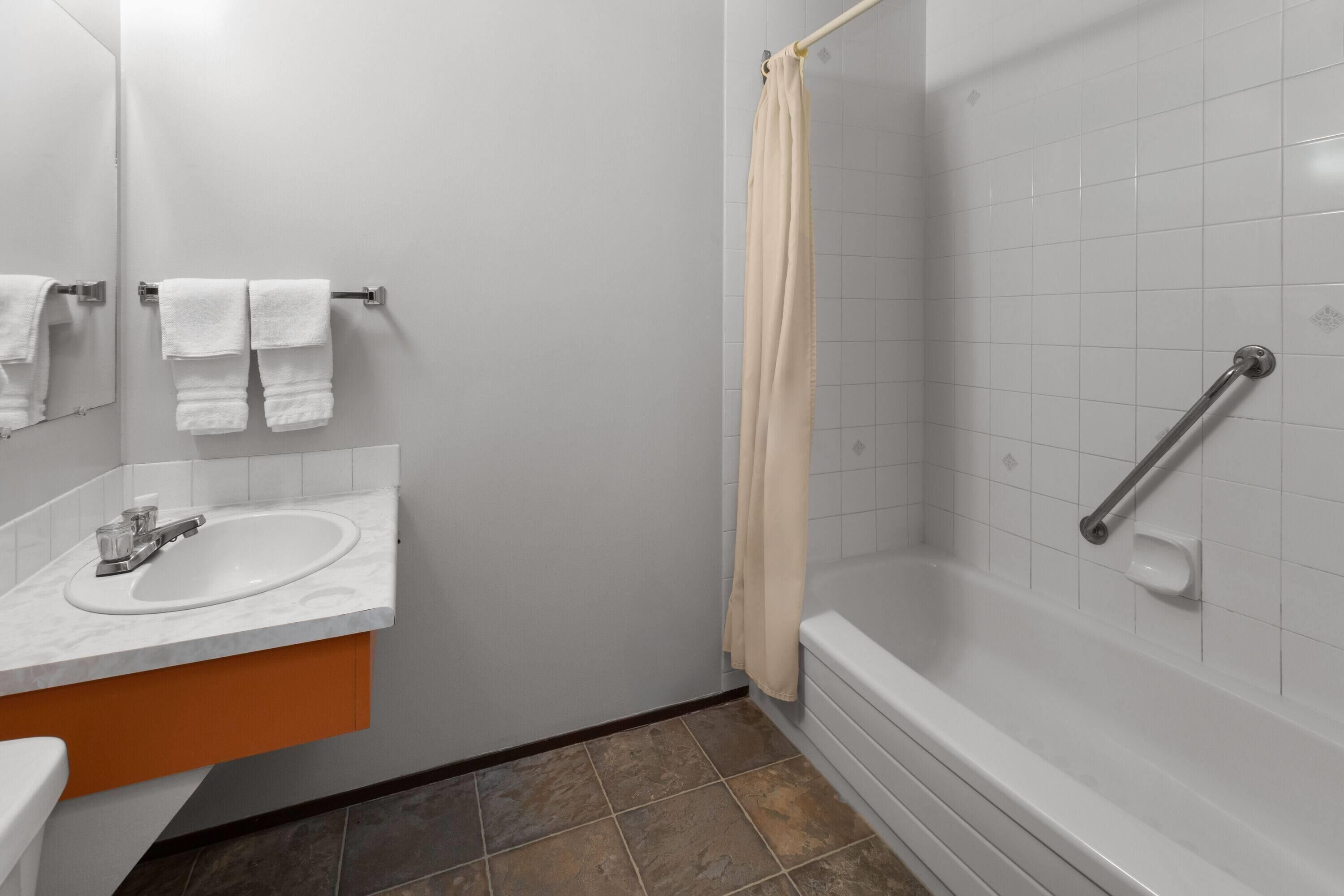 A bathroom with a sink, mirror, towel rack, shower, and grab bar.
