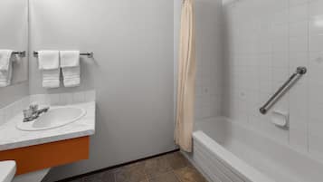 A bathroom with a sink, mirror, towel rack, shower, and grab bar.