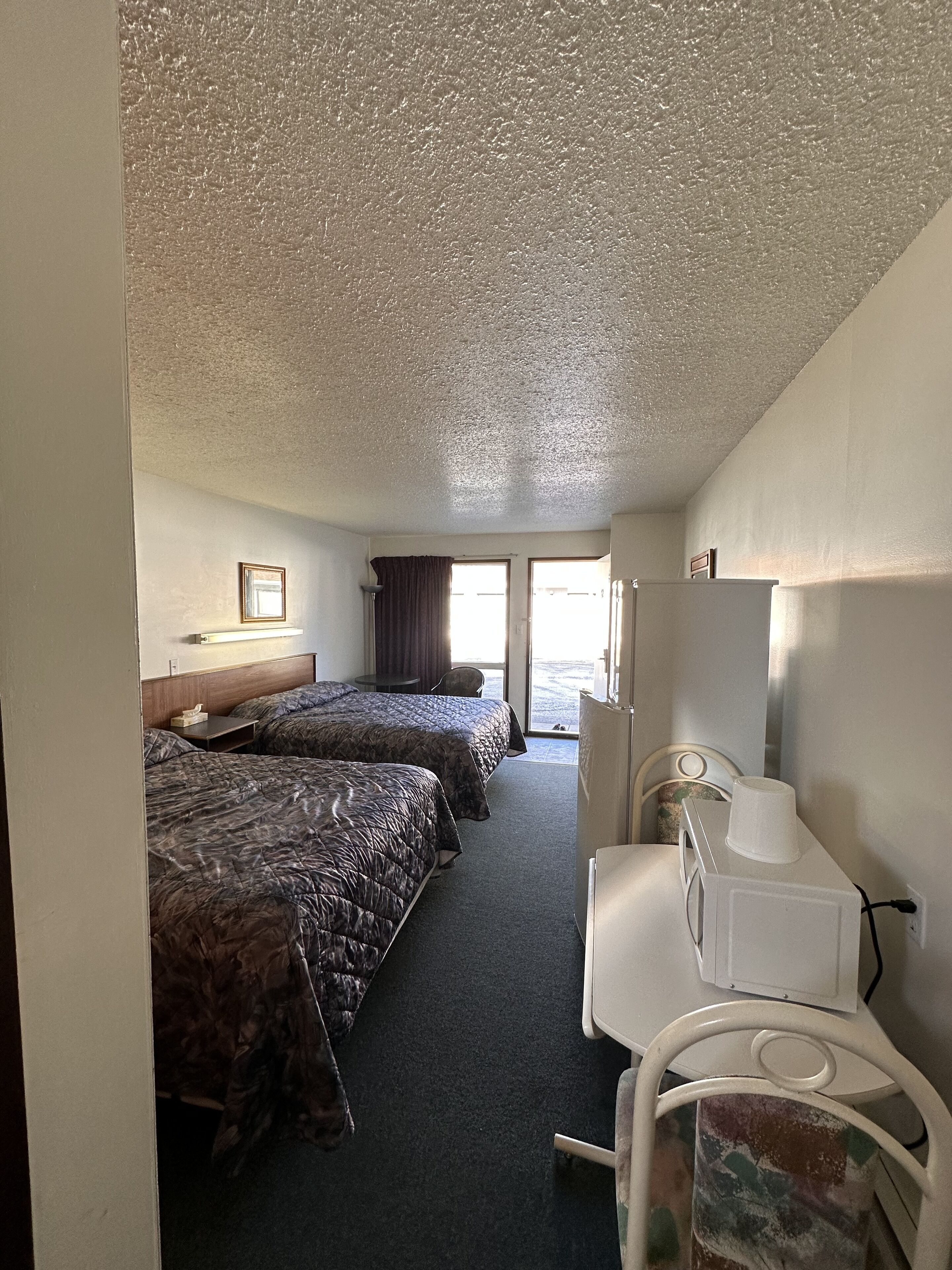A hotel room with two beds, a desk, a chair, and a refrigerator.