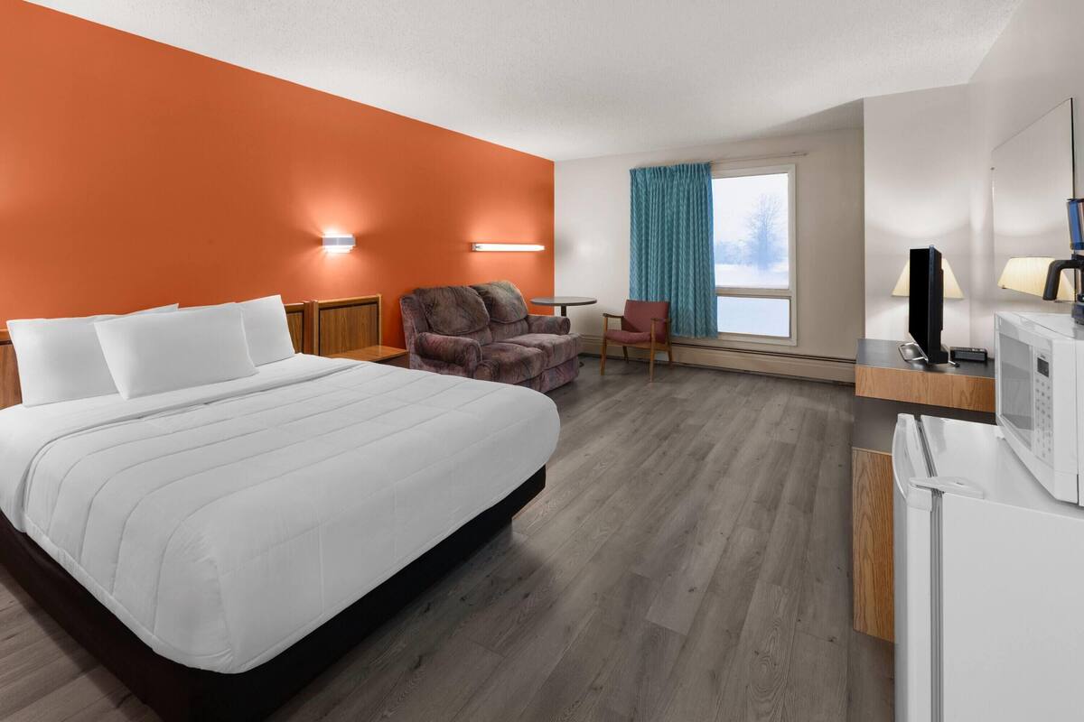 A hotel room with a bed, a seating area with a chair and a table, a TV, and a microwave.