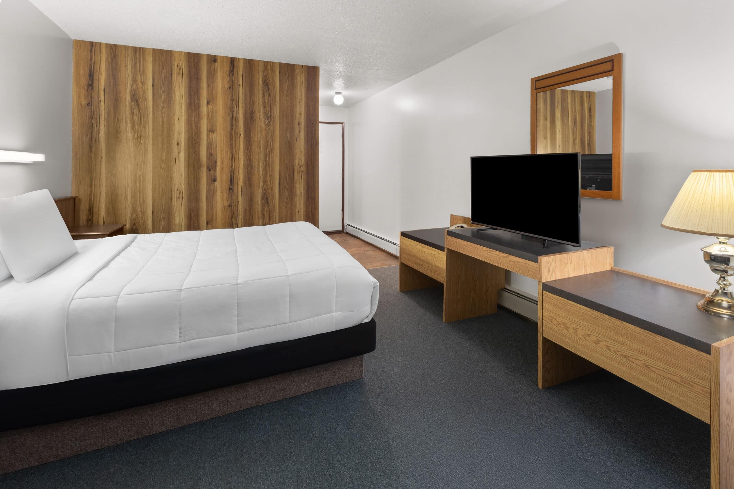 A modern hotel room with a bed, a desk, a television, and a mirror.