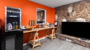 Cucina con parete in pietra, frigorifero, sgabello da bar in legno e televisore a schermo piatto.