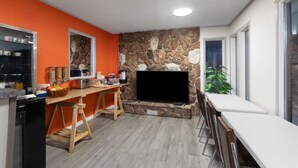 Cucina con parete in pietra, TV e zona pranzo con sedie.
