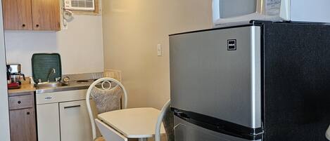 A compact kitchen with a refrigerator, microwave, and a small dining area with a chair and table.